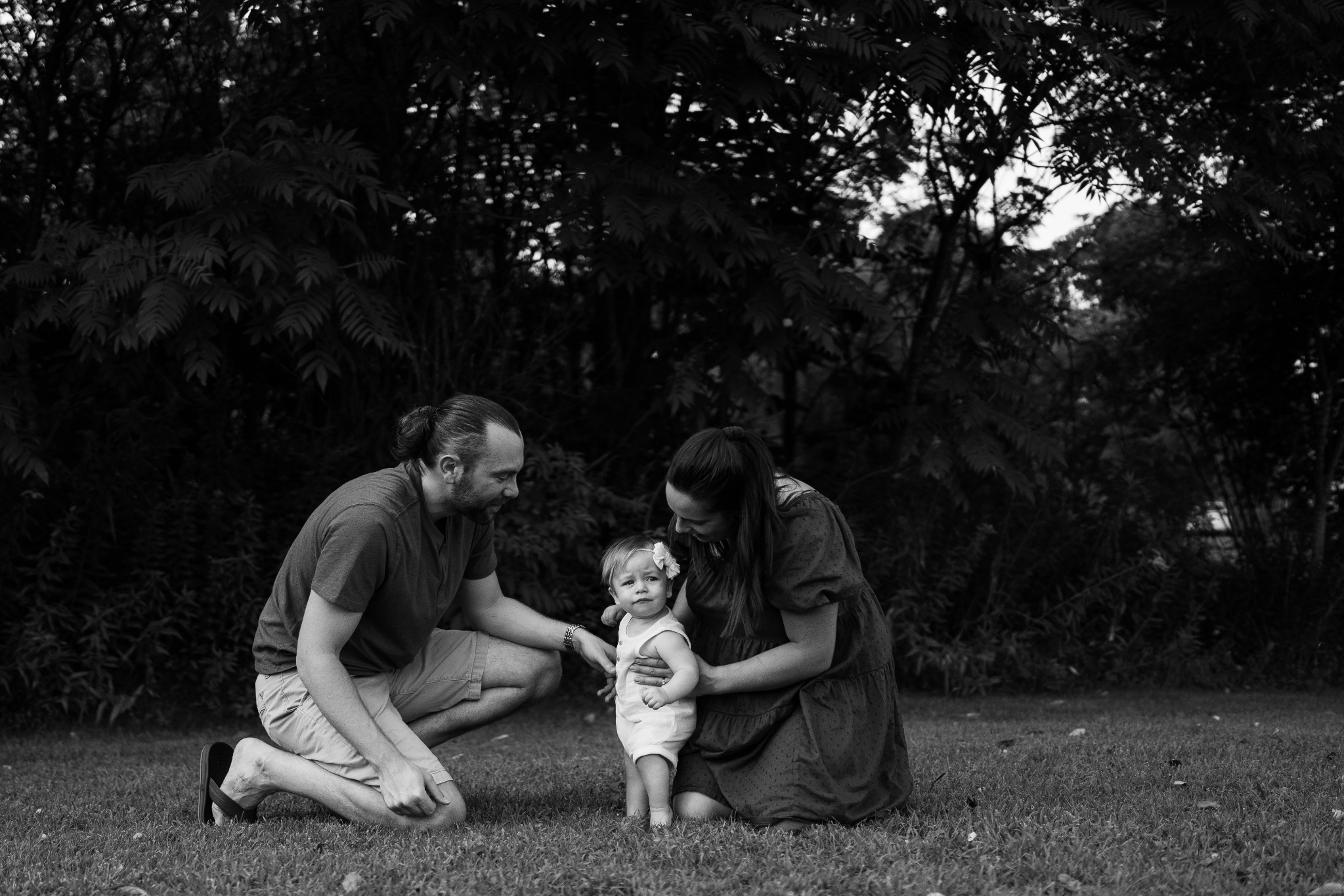 A black and white photograph of parents kneeling beside their young daughter in a garden